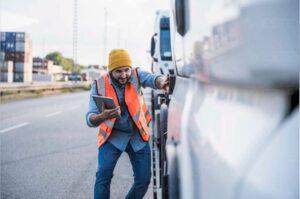 Truck driver holding a tablet and inspecting his truck while wondering how he can get started with his truck accident case.